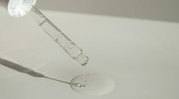 Glass dropper releasing serum on white surface