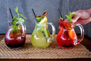 Three fruit cocktails in glass pitchers with garnishes