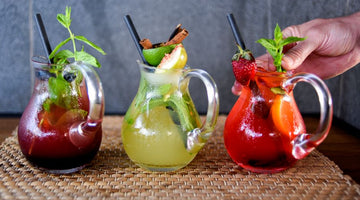 Three fruit cocktails in glass pitchers with garnishes